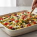 One-pan Mediterranean quinoa bake with tomatoes, olives, feta, and fresh herbs, photographed in bright natural light.