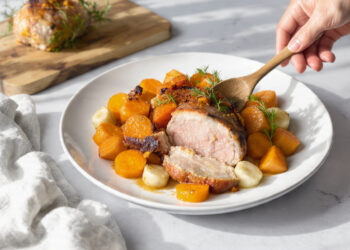 One-pan roasted pork tenderloin with fall root vegetables, carrots, and sweet potatoes on a dark baking sheet.