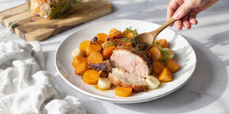 One-pan roasted pork tenderloin with fall root vegetables, carrots, and sweet potatoes on a dark baking sheet.