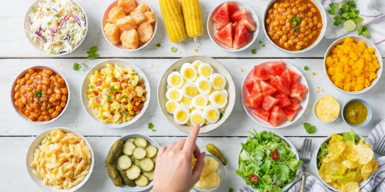 A spread of 15 colorful cookout side dishes including pasta salad, coleslaw, and grilled vegetables on a picnic table