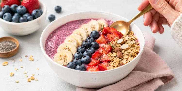 Easy summer smoothie bowl topped with fresh berries, granola, and sliced banana in a white bowl