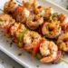 Grilled shrimp kabobs with colorful bell peppers on skewers, served on a white plate