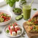 Healthy summer recipes under 30 minutes with salad, avocado toast, fruit skewers, and green smoothie on marble.