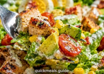 Summer chicken salad with grilled chicken, mixed greens, cherry tomatoes, and cucumber in a white bowl on a neutral background.