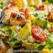 Summer chicken salad with grilled chicken, mixed greens, cherry tomatoes, and cucumber in a white bowl on a neutral background.