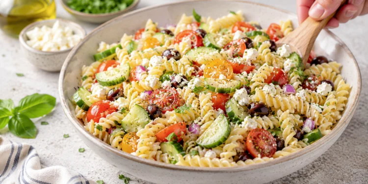 Summer pasta salad with feta cheese, cherry tomatoes, cucumber, and olives in a light lemon vinaigrette