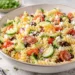 Summer pasta salad with feta cheese, cherry tomatoes, cucumber, and olives in a light lemon vinaigrette