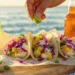 Grilled fish tacos with cabbage slaw, avocado slices, and lime on soft tortillas