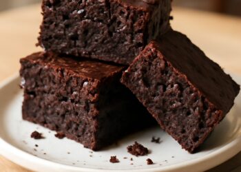 A stack of three fudgy zucchini brownies with a rich chocolate color and slightly crackled top, dusted with powdered sugar