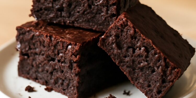 A stack of three fudgy zucchini brownies with a rich chocolate color and slightly crackled top, dusted with powdered sugar