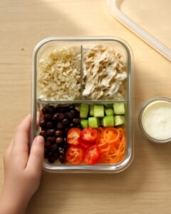 Colorful bento-style lunch box with pasta salad, fresh fruit, cheese, and crackers