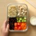 Colorful bento-style lunch box with pasta salad, fresh fruit, cheese, and crackers