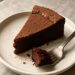 A slice of rich flourless chocolate cake with a fudgy center on a white plate