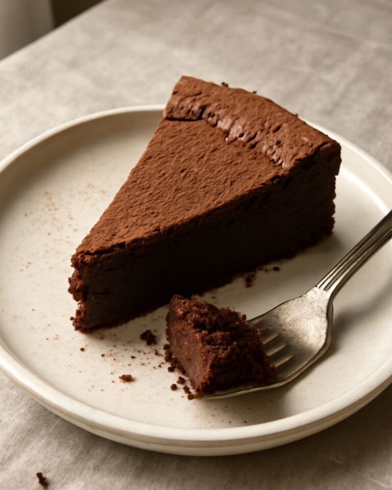 A slice of rich flourless chocolate cake with a fudgy center on a white plate